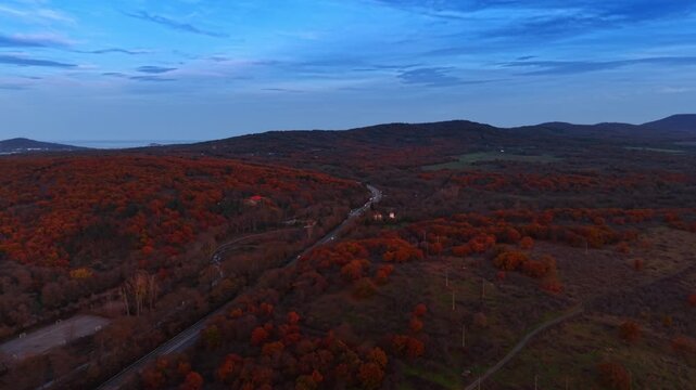 Winding road through autumn hills near Black Sea coast. Curving highway amid orange and red forest with distant mountains and overcast sky.