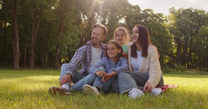 Happy family warm sunny summer day family portrait fun, parents, small children play together on green grassy area in park, enjoying summer holiday outdoors, smiling during fun and sport weekend