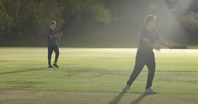 Male teenage bowler delivering ball on pitch causing fielder catching, teammates celebrating