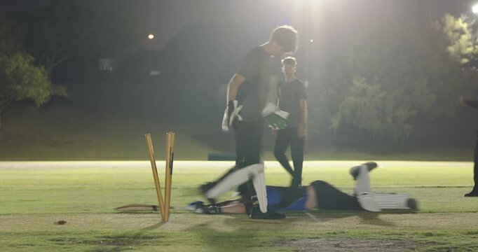 Cricket fielders and umpire appealing, celebrating wicket, bowler delivering ball under lights