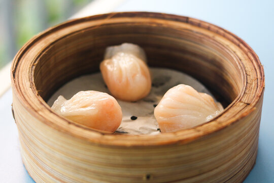Closeup view of steamed har gow dumplings served in a bamboo basket, with translucent wrappers showing the shrimp filling inside.