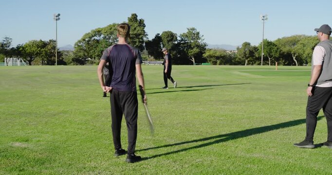 Coach underarming ball to teen player batsman on pitch causing miss, fielder collecting ball