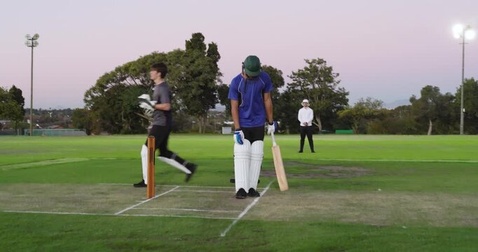 Receiving throw from fielder on pitch, dusk, teenage batsman adjusting stance facing next ball