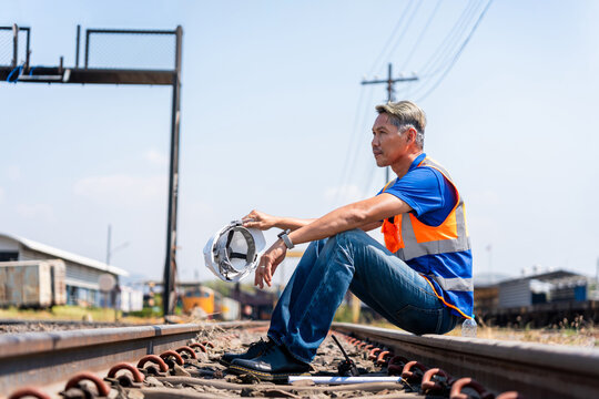 Railway engineer resting on train tracks during maintenance work, Railroad worker sitting on tracks at industrial terminal, Infrastructure maintenance technician taking a break on railway line