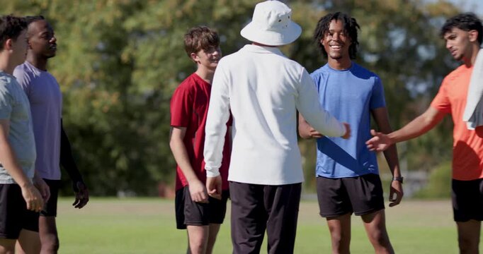 Coach and team members pausing on grass sports field, with bucket hat, towel, wristwatch