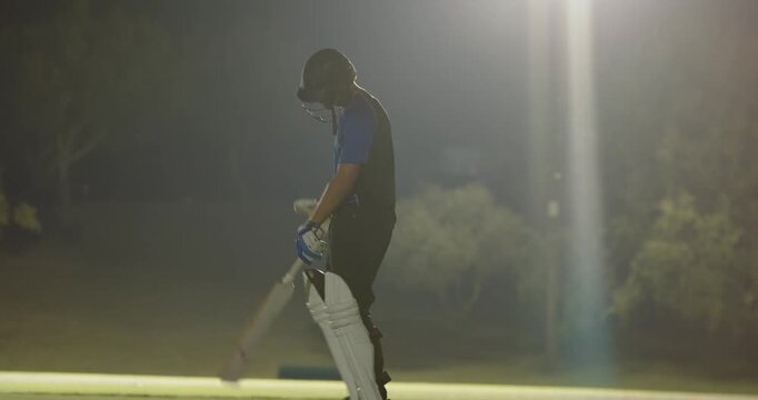 After delivery, male teammates tapping bats walking on pitch under lights to resume innings
