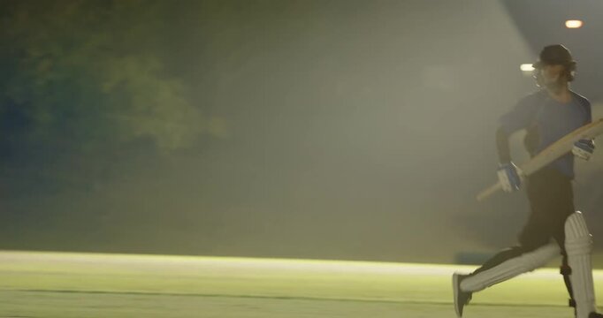 Male batsman facing bowler driving ball past keeper sprinting run preparing guard with floodlights