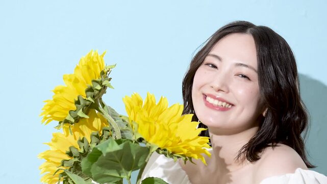 [スローモーション]水色背景でひまわり(向日葵)の花束を持って笑顔の女性カメラ目線　 爽やかな真夏のイメージのファッション動画