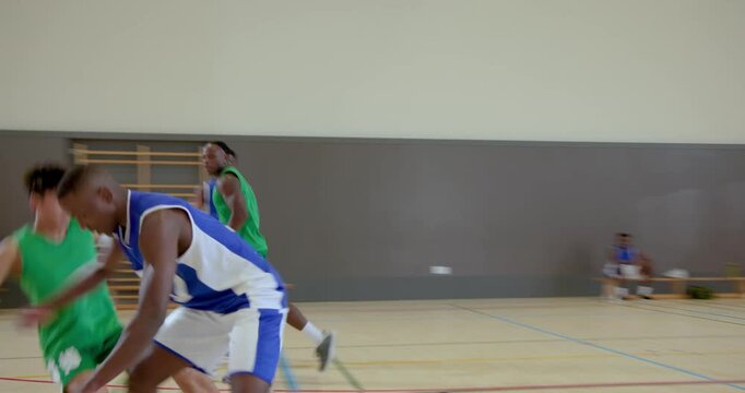 Passing from green teammate prompting african american man dribbling toward hoop on gym court