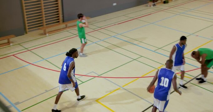 Dribbling male player falling in gym, male defenders assisting player with ball