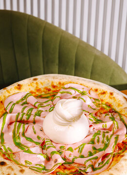 Delicious gourmet pizza topped with sliced mortadella ham and fresh burrata cheese node. Traditional Italian baked flatbread drizzled with bright green pistachio pesto sauce.