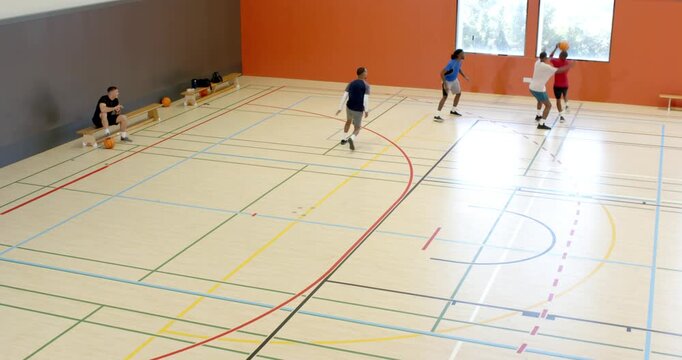 Diverse male friends picking up ball dribbling forward passing and resetting for drill in gym