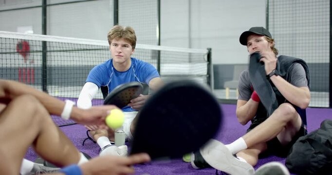 Diverse males passing paddles and balls before coach wiping forehead, showing stroke on court