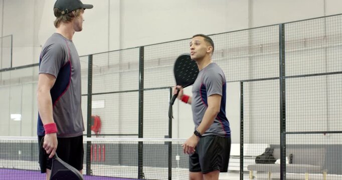 Diverse male partners planning serve and rallying until winning at net on padel court with ball