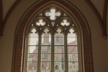 Obraz premium A serene view of a historic Gothic cathedral through a stunning stained glass window in Toruń's Copernicus Birthplace.