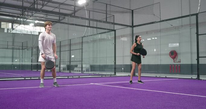 Diverse friends tossing ball and volleying for training on purple padel court with rackets