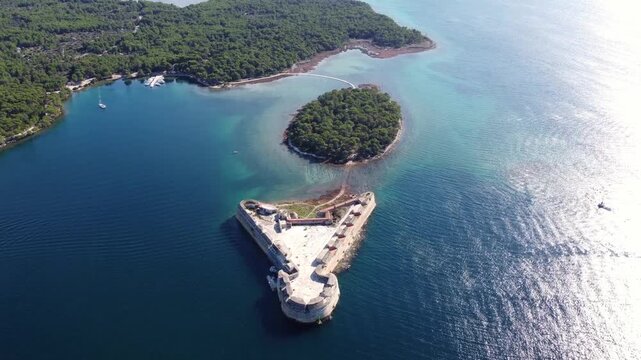 Cinematic straight steady drone video of St. Nicholas Fortress on the Adriatic coast near &Scaron;ibenik, Croatia. The historic stone fortress is surrounded by clear blue sea, turquoise water, pine forest.