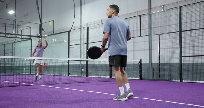 Diverse male athletes bouncing ball spurring volleying and returning serve on paddle court