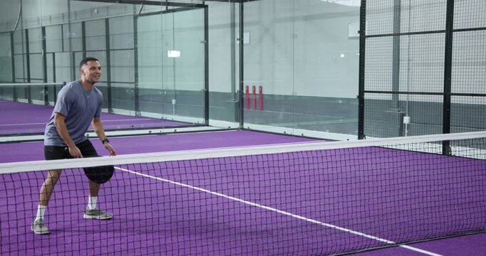 Diverse male opponents rallying ball on padel court, gathering balls and resuming serve