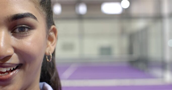Indian woman showing focus shifting into slight smile on tennis court with net, copy space