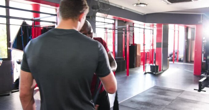 African american coach unrolling black wrap, guiding trainee wrapping hand at gym for warmup