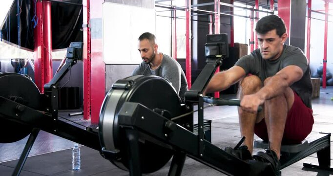 Diverse male friends starting catch drive on rowers intensifying strokes at gym