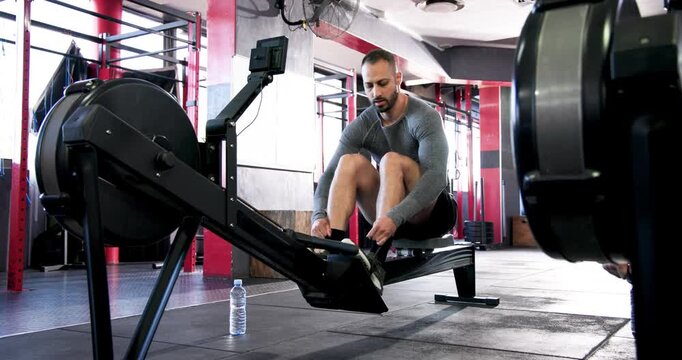 Diverse gym mates securing foot straps on ergometer and rowing in unison for gym workout