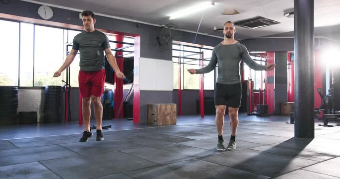 Diverse male friends swinging ropes jumping two-foot and alternating high-knee skips in gym