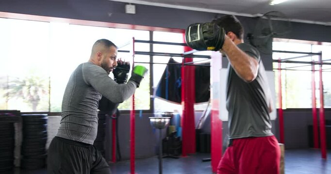 Trainer raising focus mitts urging boxer trainee throwing jab-cross combos for skill at boxing ring
