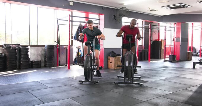 Diverse male friends mounting air bikes, gripping handles, pedaling to finish tough interval