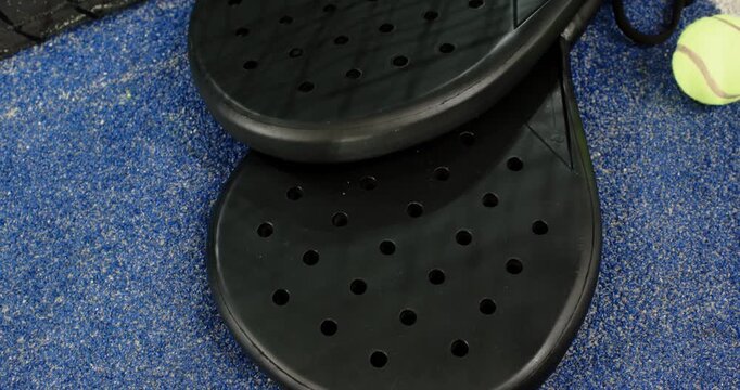 At four-second mark camera is panning up from padel rackets revealing tennis ball and net