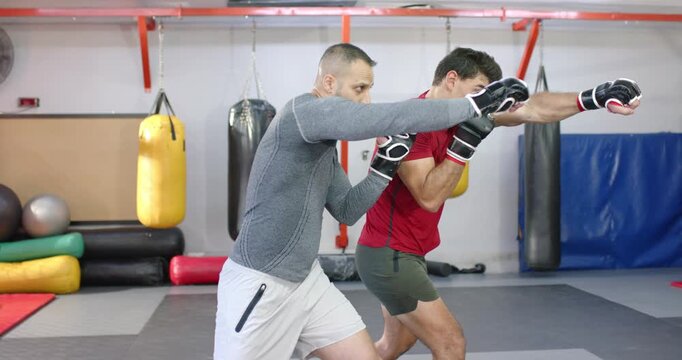 After cue diverse male coach and trainee throwing jab and cross sequences at gym