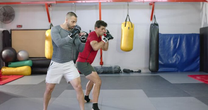 Grey-shirt cueing left jab, diverse men training partners executing jab-cross mat drills