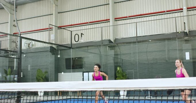 Diverse female doubles teammates volleying incoming ball on padel court celebrating win