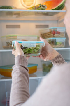 Woman Storing Healthy Meal Prep Containers in Refrigerator at Home. Close up