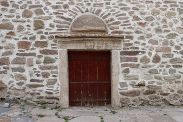 Fototapeta premium A wall made of rubble stone. In the middle of the wall is an old brown wooden door.