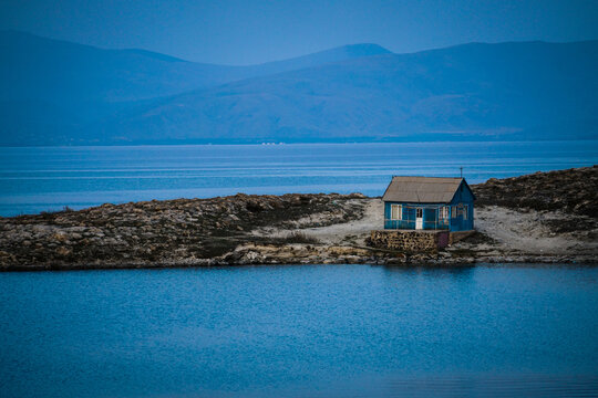 Isolated blue house on the rocky shores of Lake Sevan in Armenia, under a tranquil twilight sky.
