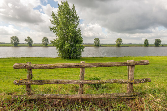 Weathered old wooden fence in the foreground of a Dutch landscape with a river. The photo was taken on a heavily overcast day at the end of the spring season.