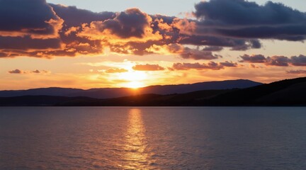 Fototapeta premium Sunset over a tranquil lake with rolling hills and colorful clouds. Sun dips below horizon, reflecting golden light on water surface. Peaceful evening scene offers natural beauty and quiet.