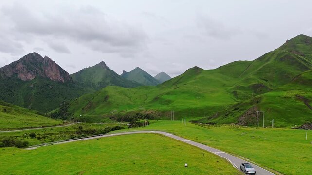 Aerial view of car driving on winding road through lush green grasslands and mountains in Gannan, Gansu, China