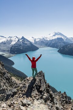 View from Panorama Ridge Hiking Trail, Hiker on a rock stretches arms into the air, Garibaldi Lake, Turquoise Glacial Lake, Guard Mountain and Deception Peak, Glacier, Garibaldi Provincial Park, British Columbia, Canada