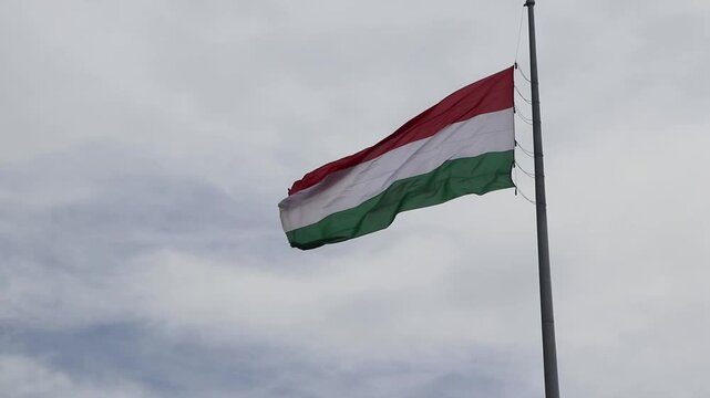 Low-angle shot of the national flag of Hungary blowing in the wind at the historic Citadella fortress in Budapest, against a cloudy sky