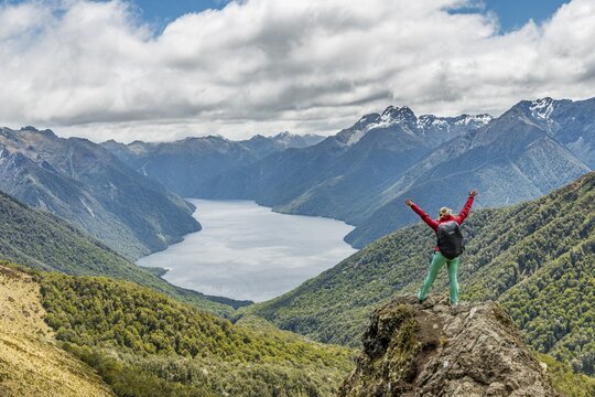 Female hiker looking at the South Fiord of Lake Te Anau, arms outstretched, Southern Alps at back, hiking trail Kepler Tack, Fiordland National Park, Southland, New Zealand