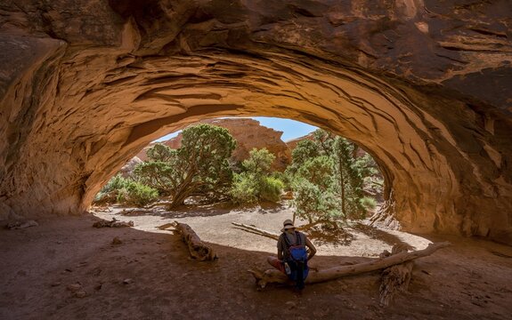 Young man sitting under rock arch, Navajo Arch, Devils Garden, Arches National Park, Moab, Utah, USA