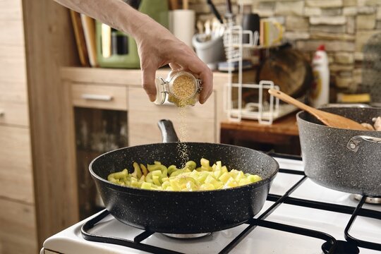 A hand pours crushed dry garlic over a pan filled with chopped vegetables