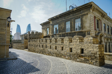 Naklejka premium Ancient stone wall and cobblestone street in Baku's Old City, with distant modern Flame Towers.