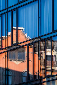 Brick building and windows appear inside blue glass reflection, turning a facade into abstract urban architecture across dark lines