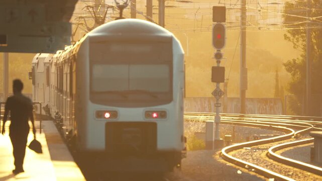 Train arrives at station during sunset while passenger walks along platform