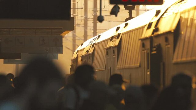 Train arrives at station during evening rush hour with people waiting and boarding in a busy atmosphere