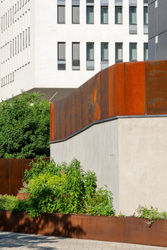 A rust metal wall with green shrubs frames a building exterior, where sustainable architecture adds landscape planting beside the facade